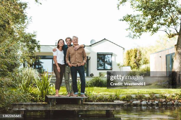 smiling family standing together on jetty by lake at backyard - familie eigenheim stock-fotos und bilder