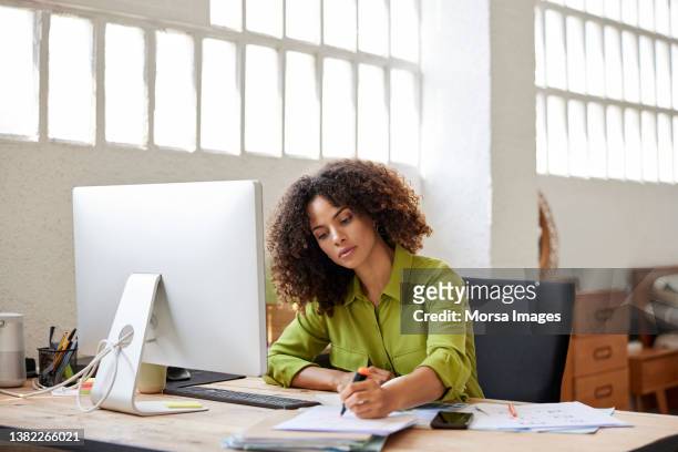businesswoman writing on document sitting at desk - papierkram stock-fotos und bilder
