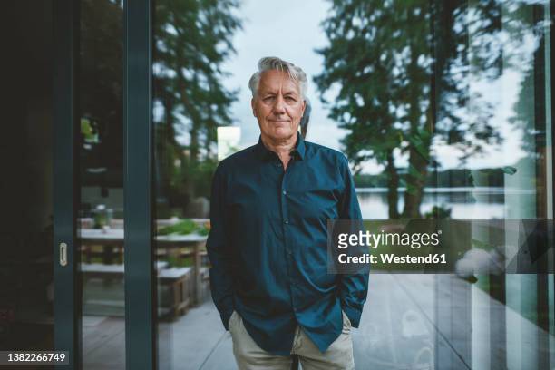 senior man with hands in pockets standing in front of glass wall - old rich man stock pictures, royalty-free photos & images