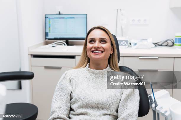 smiling young woman sitting on dentist chair at clinic - dentists chair stockfoto's en -beelden