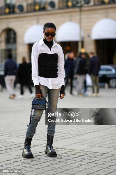 Guest wears black sunglasses, gold pendant earrings, a black wool ribbed turtleneck pullover, a white shirt, a black corset, blue and yellow faded...