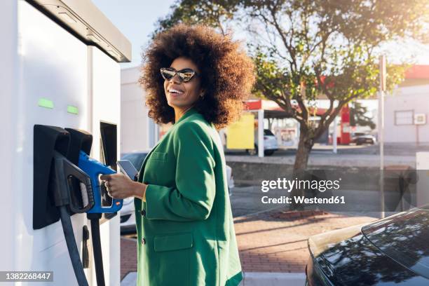 happy businesswoman with fuel pump at gas station - ガソリンスタンド ストックフォトと画像