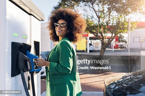 Happy businesswoman with fuel pump at gas station Happy businesswoman with fuel pump at gas station