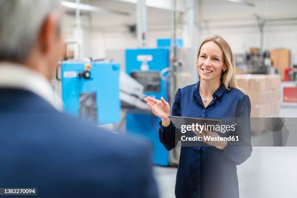 smiling blond businesswoman holding tablet pc discussing with colleague in factory - 40 44 years blond hair mature man factory stock pictures, royalty-free photos & images