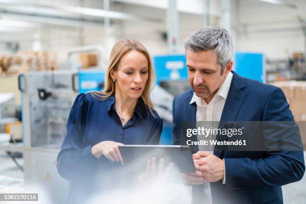 blond businesswoman sharing tablet pc with colleague in factory - 40 44 years blond hair mature man factory stock pictures, royalty-free photos & images