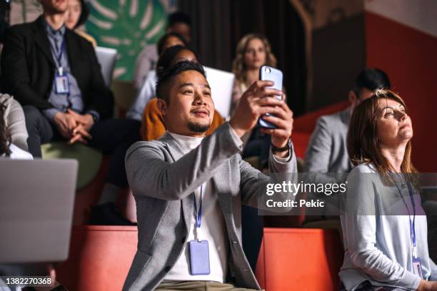 giovane uomo ben vestito che scatta una foto mentre partecipa alla conferenza di lavoro - photo messaging foto e immagini stock