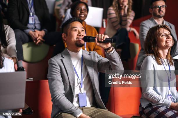 well dressed young man asking presenter a question while attending business conference - attending stock pictures, royalty-free photos & images