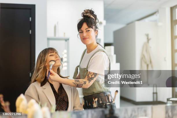 smiling beautician applying blush to woman at beauty salon - schoonheidsspecialist stockfoto's en -beelden