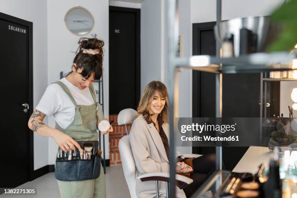 happy make-up artist talking with customer sitting on chair at salon - esthetician stock pictures, royalty-free photos & images