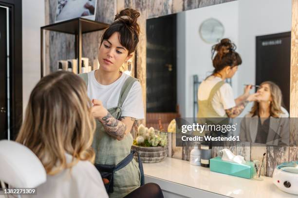 beautician applying make-up on woman's face at salon - esthéticienne photos et images de collection