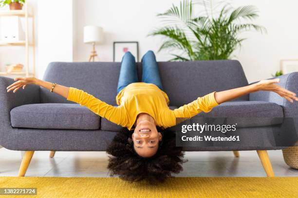 happy young woman lying upside down on sofa in living room at home - upside down stock pictures, royalty-free photos & images