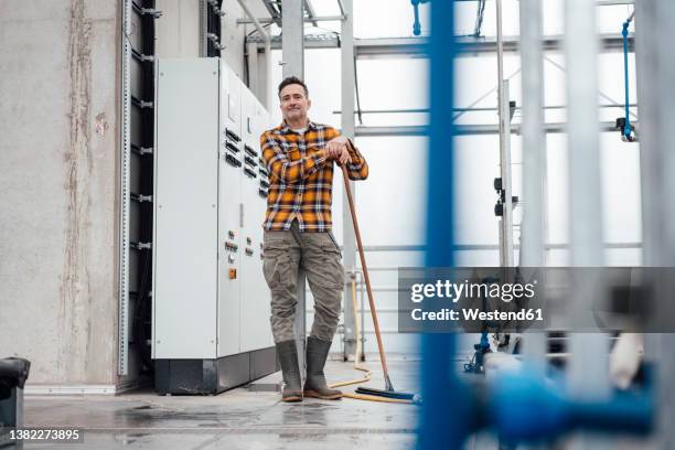 employee wearing rubber boots standing with mop in greenhouse - rubber boots stock-fotos und bilder