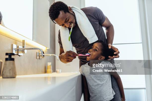 father brushing teeth of daughter in bathroom at home - brushing teeth stock pictures, royalty-free photos & images