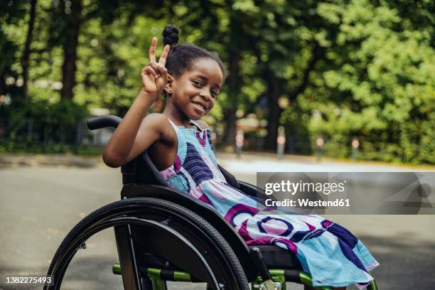 disabled girl in wheelchair making peace sign - child with disability photos et images de collection