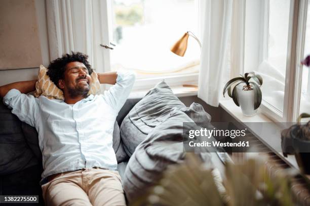 smiling man with eyes closed resting on sofa at home - man resting stock pictures, royalty-free photos & images