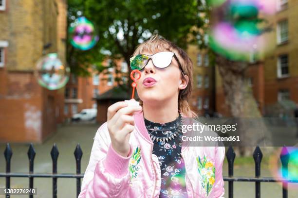 young woman wearing sunglasses blowing soap bubbles - blowing bubbles stock pictures, royalty-free photos & images