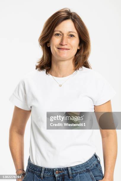 smiling woman standing with hands in pocket against white background - white t shirt fotografías e imágenes de stock