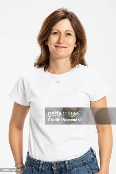 smiling woman standing with hands in pocket against white background - 40s woman t shirt studio stock pictures, royalty-free photos & images