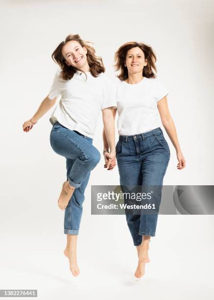 playful mother and daughter jumping in studio - white t shirt studio imagens e fotografias de stock