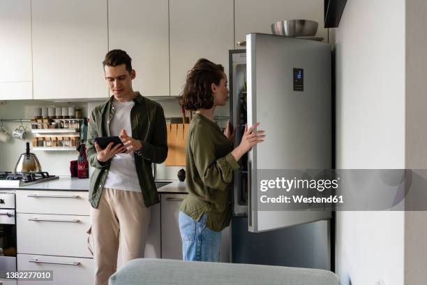 young man using tablet pc by woman opening refrigerator in kitchen at home - smart kitchen stock pictures, royalty-free photos & images