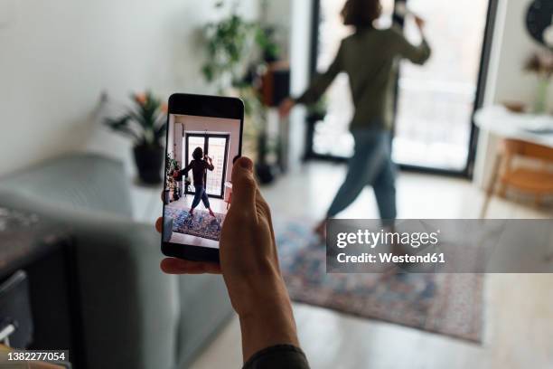 man photographing singing girlfriend through mobile phone at home - baby dancing stock-fotos und bilder