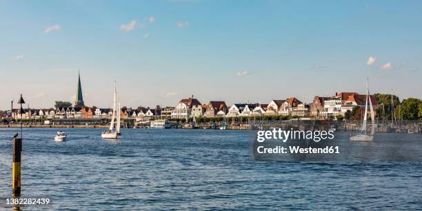 germany, schleswig-holstein, lubeck, boats on river trave with townhouses in background - travemünde stockfoto's en -beelden