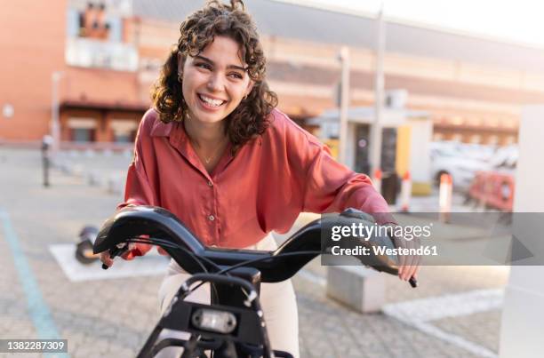 happy woman riding electric bicycle at station - ebike stock pictures, royalty-free photos & images
