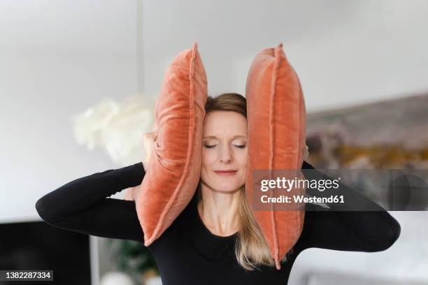 woman covering ears with pillows at home - hand to ear photos et images de collection