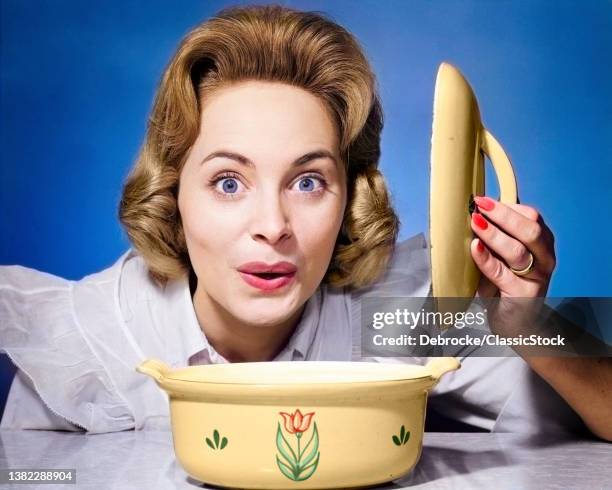 1960s 1950s Surprised Happy Woman Housewife Cook Lifting The Lid Off Of Casserole Dish Looking At Camera.