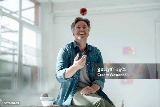 smiling man throwing apple sitting on table - man catching stock pictures, royalty-free photos & images