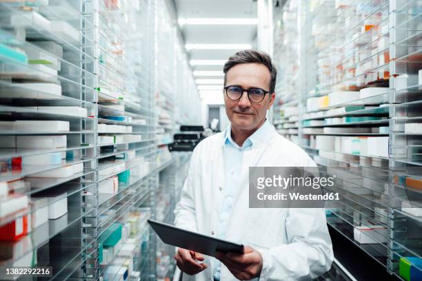 pharmacist with tablet pc standing in storage room at pharmacy - apotheker blick in kamera stock-fotos und bilder