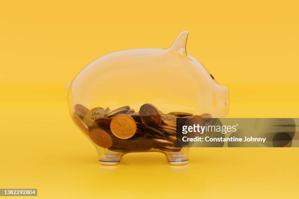 see through transparent glass piggy bank with coins on blue yellow - wages stock-fotos und bilder
