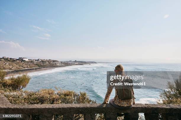 woman admiring sea sitting on railing - pais vasco stock-fotos und bilder