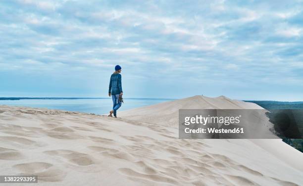 woman walking on sand dune under cloudy sky - pila stockfoto's en -beelden