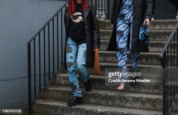 Fashion Week guests seen wearing a Coperni logo shirt, a black leather coat, a blue and black cow pattern jeans from Coperni, a brown suede Coperni...