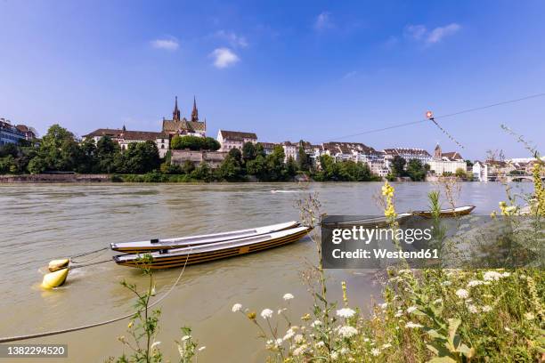 switzerland, basel-stadt, basel, rowboats moored on bank of rhine river in summer with city buildings in background - bale photos et images de collection