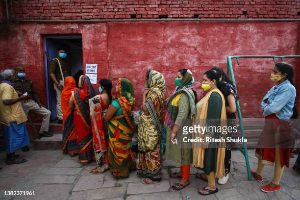 People stand in a queue to caste their votes outside a polling station during the seventh phase of state elections on March 07, 2022 in Varanasi,...