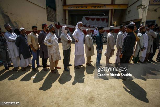 People stand in a queue to caste their votes outside a polling station during the seventh phase of state elections on March 07, 2022 in Varanasi,...