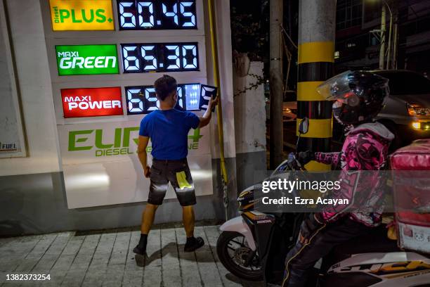 Worker adjusts the prices of fuel on a display as motorists queue at a gas station a day before a huge price increase on petroleum products is...