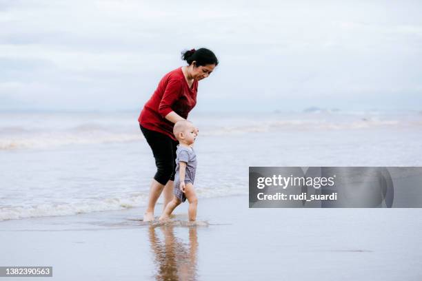 asian  mature woman teaching baby walking on the beach - chubby granny stock pictures, royalty-free photos & images