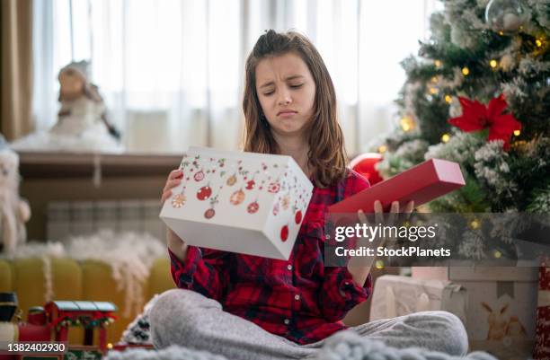 unhappy girl opening christmas present - disappointment stock pictures, royalty-free photos & images