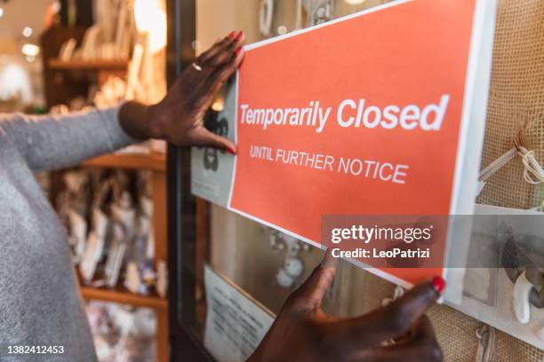 woman applying a closed sign to the entrance of a retail place due to covid-19 pandemic - state of emergency sign stock pictures, royalty-free photos & images