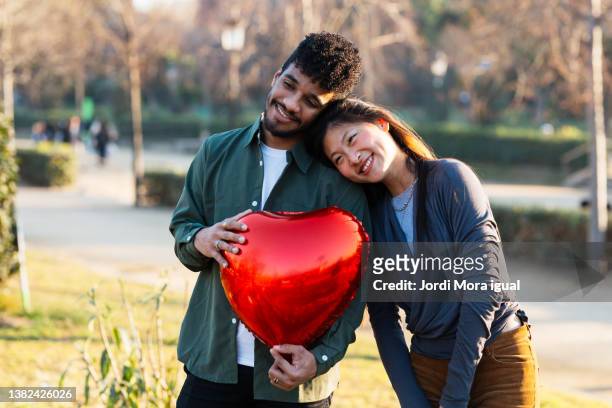 happy young couple holding red balloon in shape of heart - valentines couple stock pictures, royalty-free photos & images