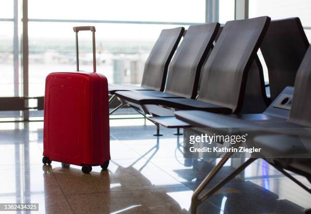 red suitcase at airport departure gate - valise stock-fotos und bilder