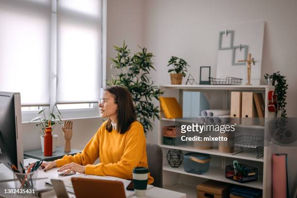 mujer emprendedora que trabaja por computadora en una pequeña oficina - yellow shirt fotografías e imágenes de stock