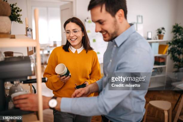 colleghi sorridenti che preparano il caffè nella caffetteria in ufficio - cafeteria foto e immagini stock