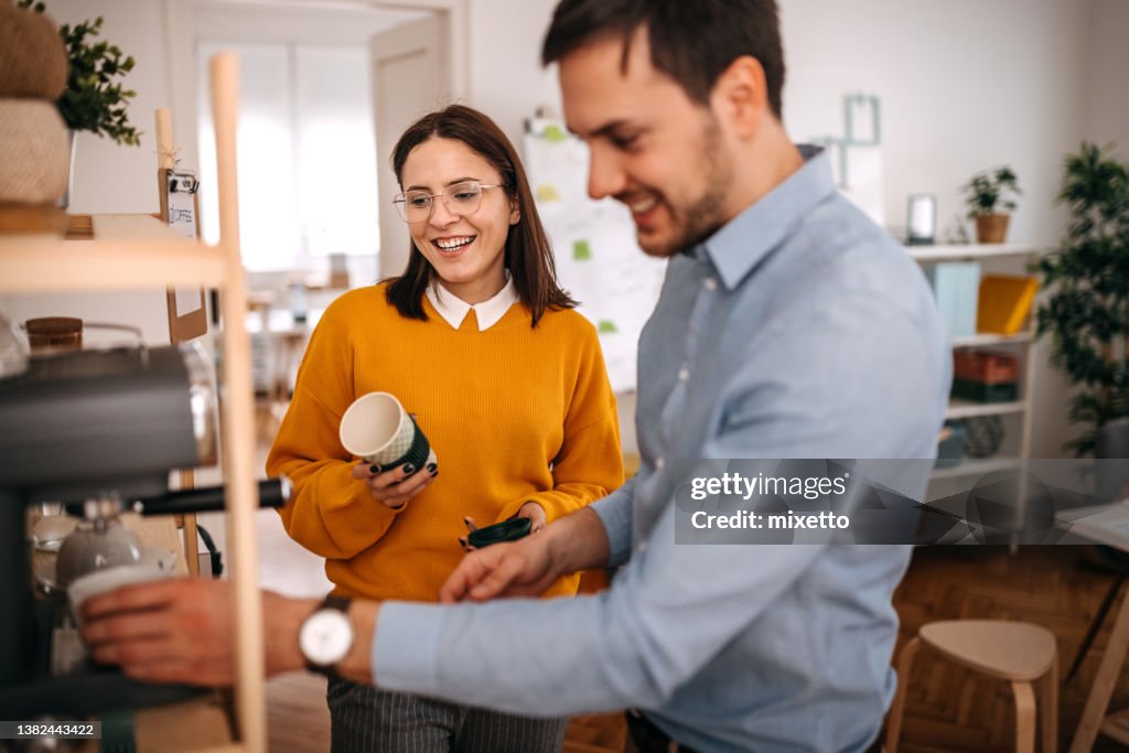Smiling colleagues making coffee in cafeteria at office