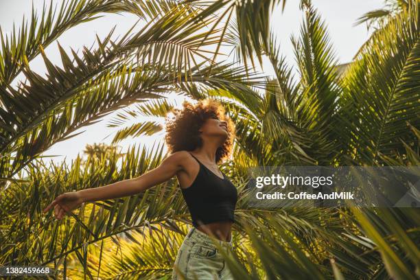 jolie jeune femme afro au milieu des palmiers - fille heureuse photos et images de collection