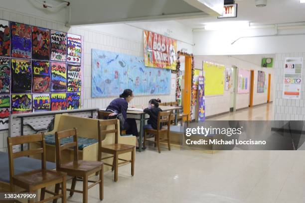 Pre-K student sits with a teacher outside a classroom at Yung Wing School P.S. 124 on March 07, 2022 in New York City. Despite the fact that masks...