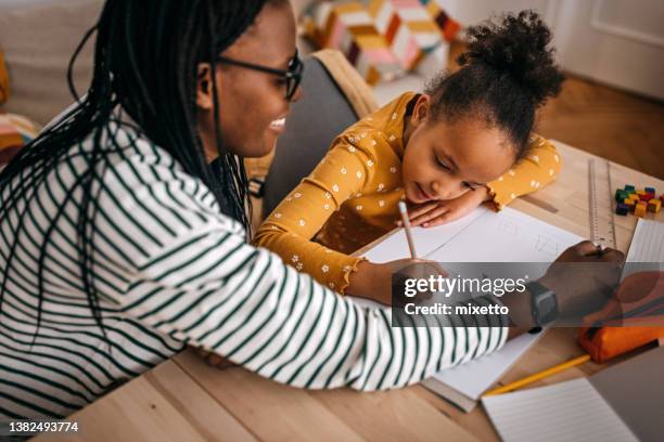 mother assisting daughter in writing homework at home - kid homework stock pictures, royalty-free photos & images